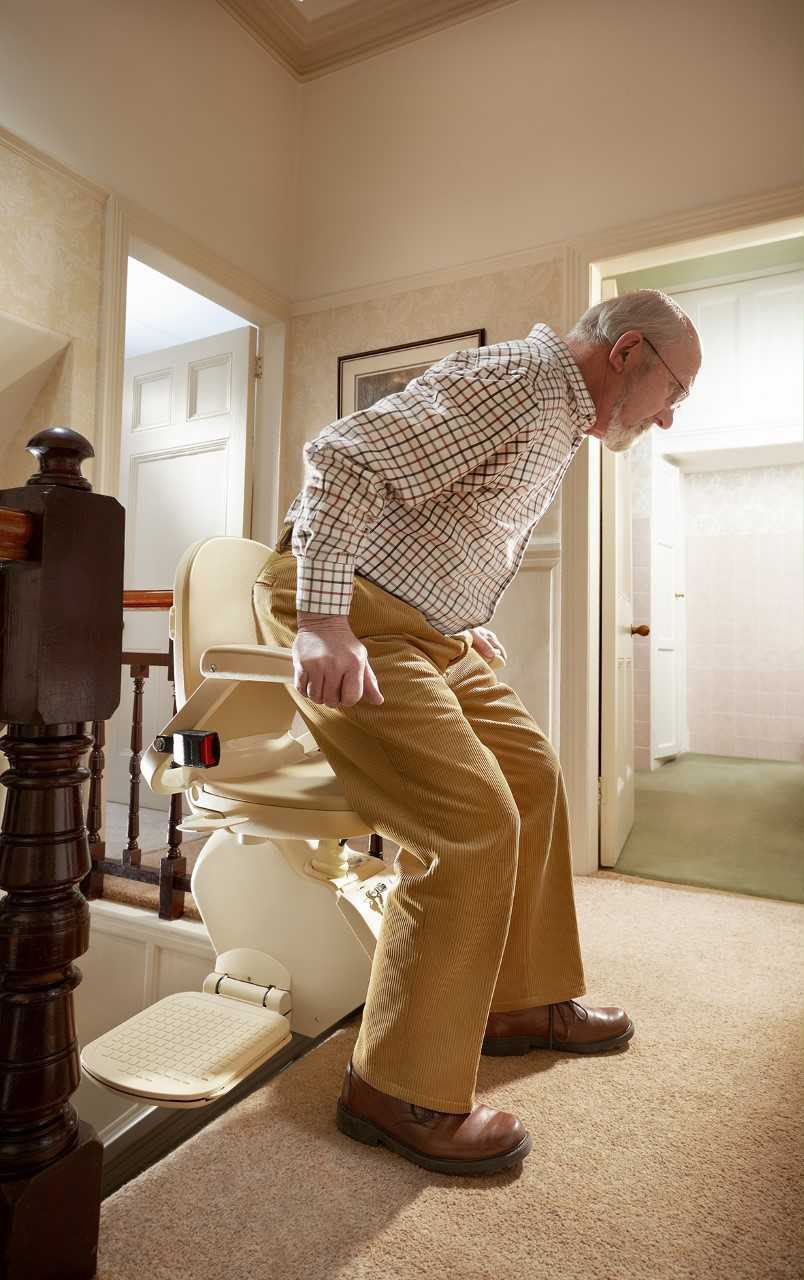 A person safely using a stairlift at the top of a home staircase